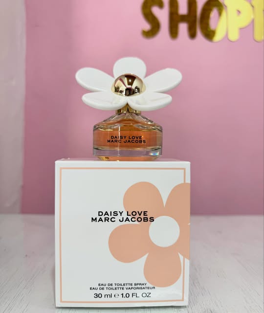 Perfume Daisy Love de Marc Jacobs sobre una caja blanca, con letras doradas al fondo.